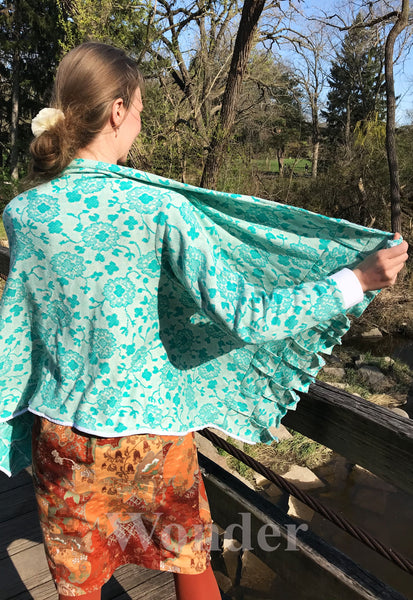 Women's mint-green cardigan with white cuffs and floral pattern shown from the backside and one side is held open.